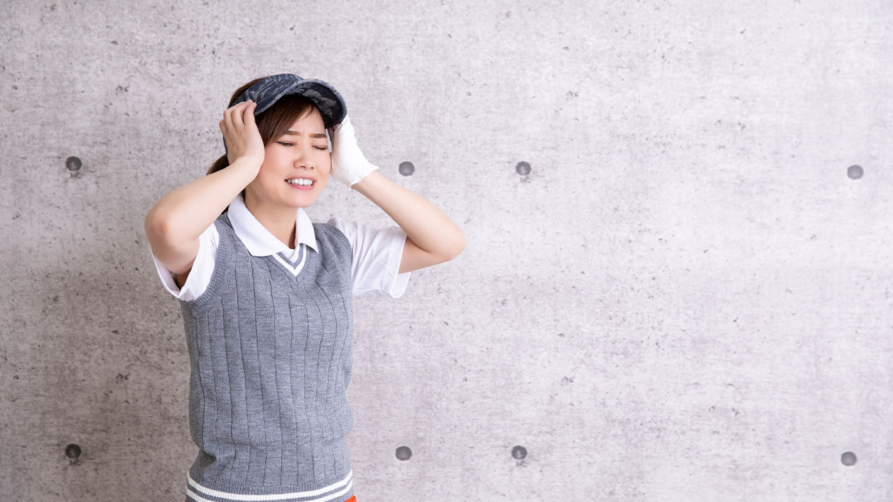 頭を抱えて悩むゴルフウェア着た女性